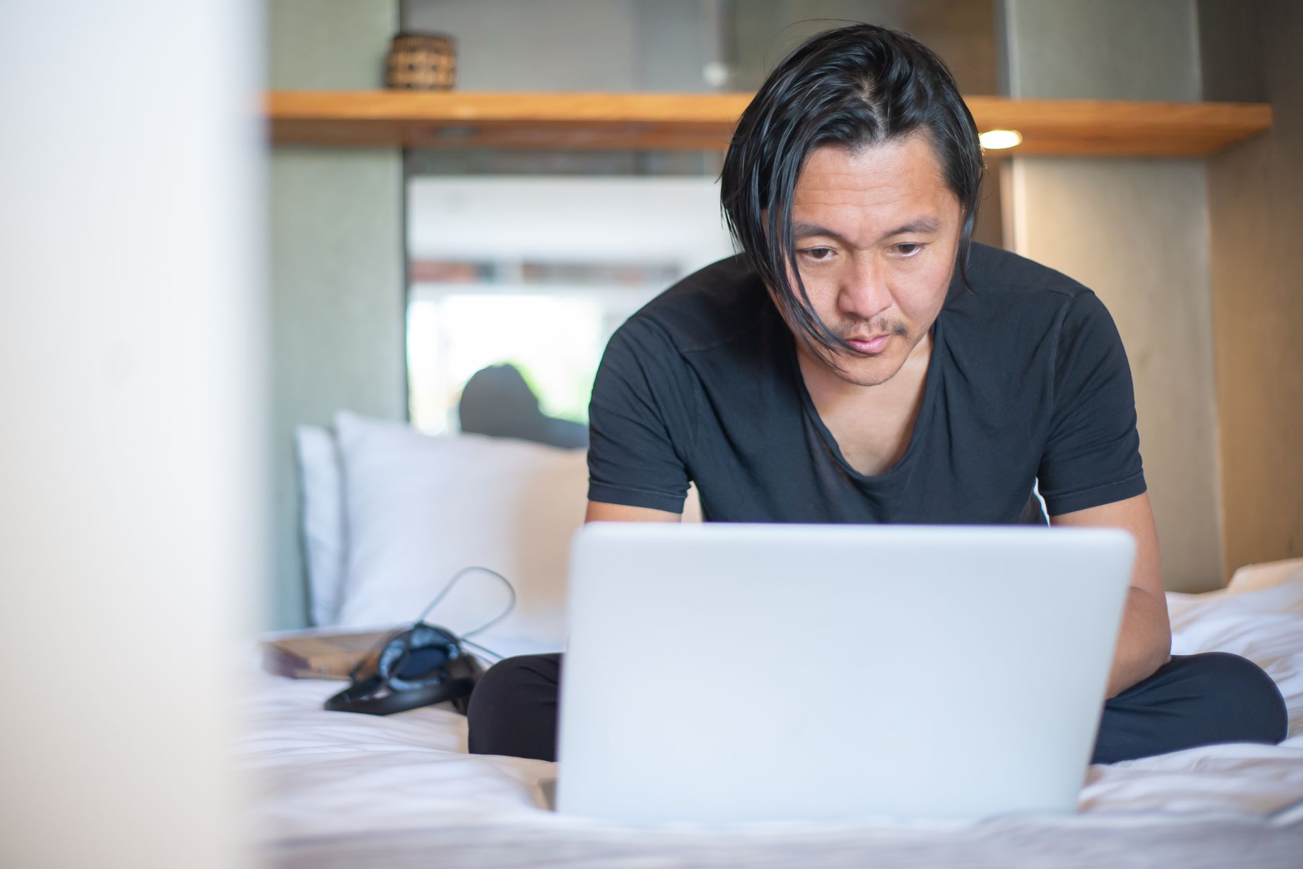 Homem trabalhando no notebook sentado na cama de casa