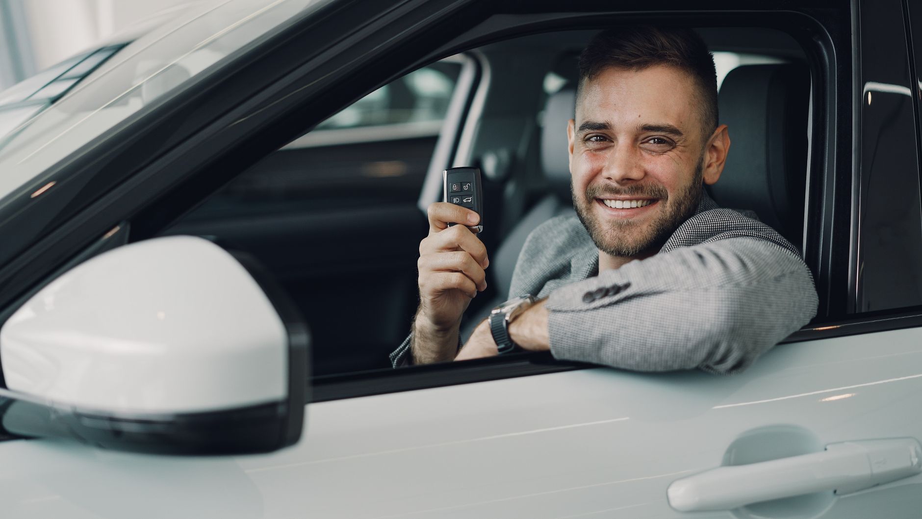 Jovem sorrindo ao volante de um carro com a janela aberta